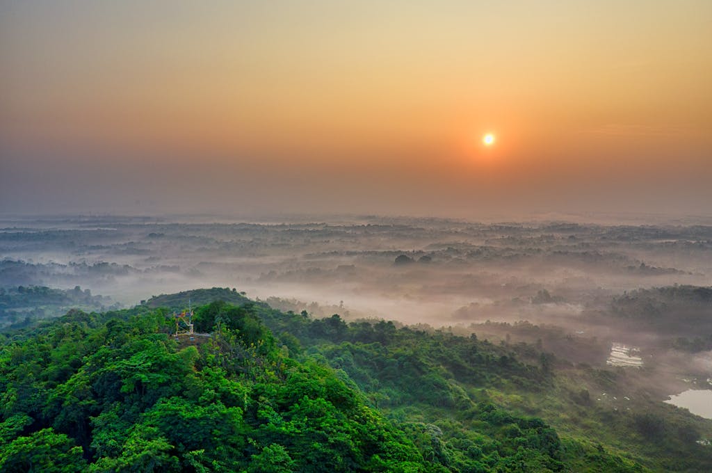 Stunning aerial view of a sunrise over a lush green landscape with mist creating a serene atmosphere.