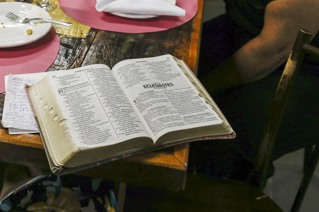 Open Bible on a wooden table with dining plates and notes, highlighting Ecclesiastes.